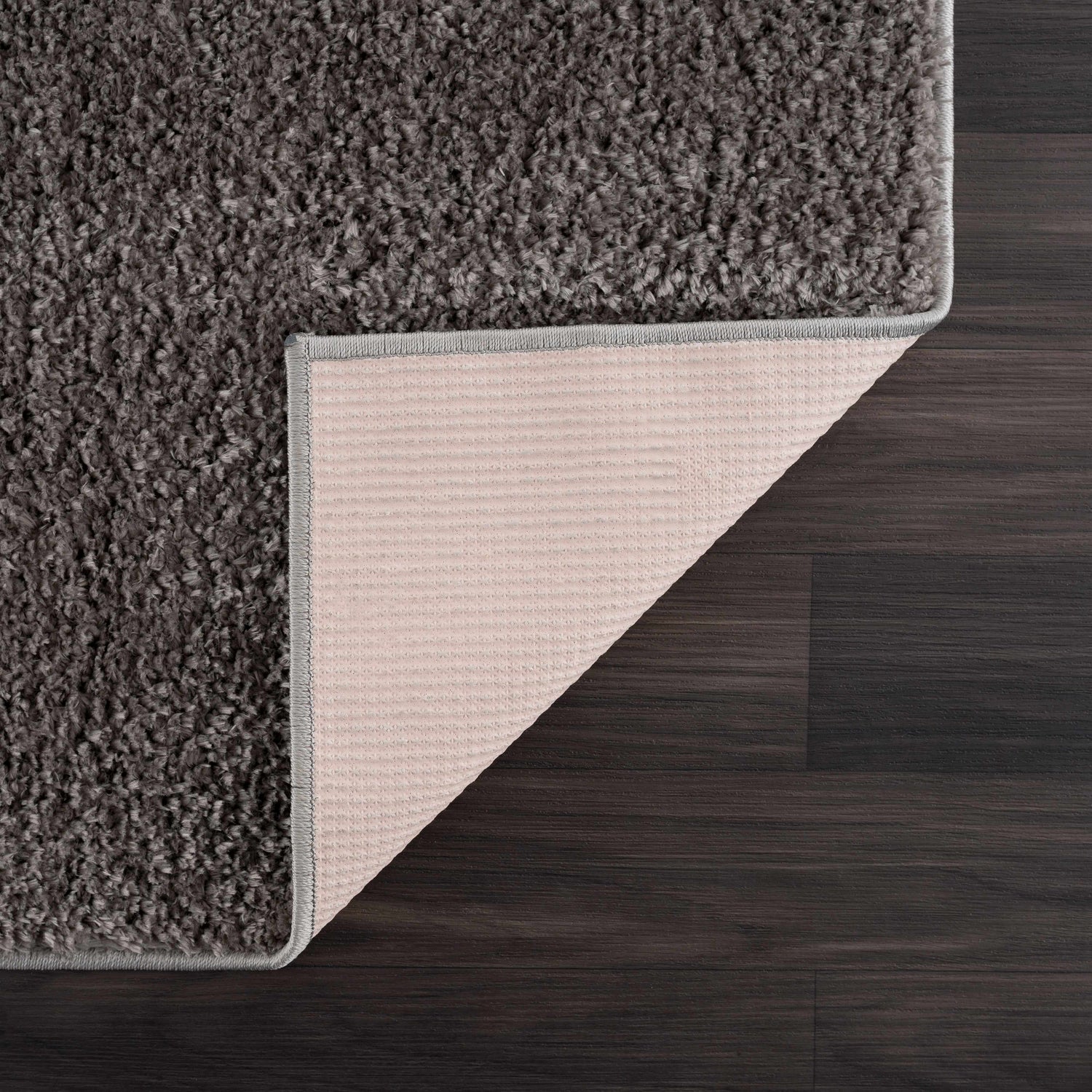 Close-up of the Judy Solid Dark Gray Washable Shag Rug showing its plush texture and non-slip backing on dark wood floor. Fold