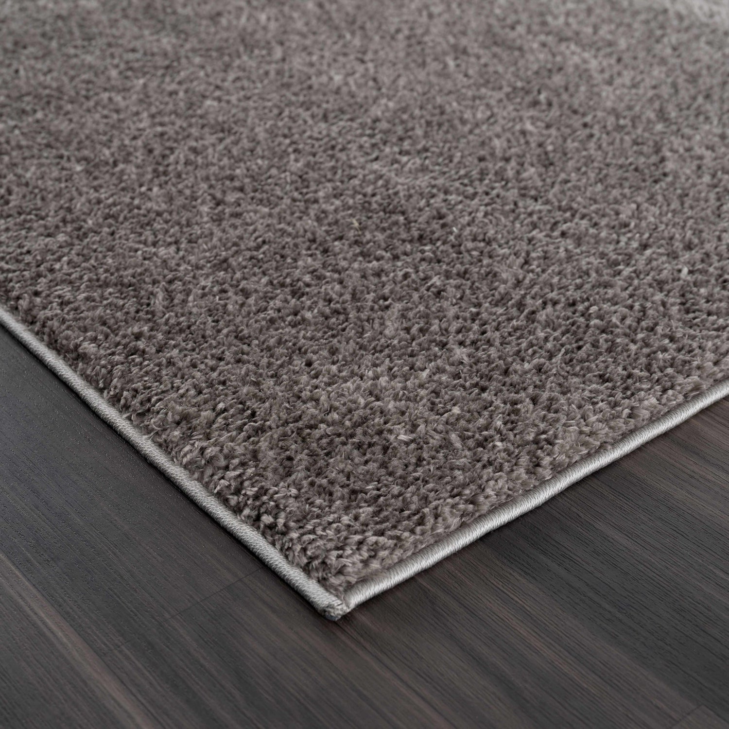 Close-up of the Judy Solid Dark Gray Washable Shag Rug showing its plush texture and dark gray color on dark wood flooring. Corner