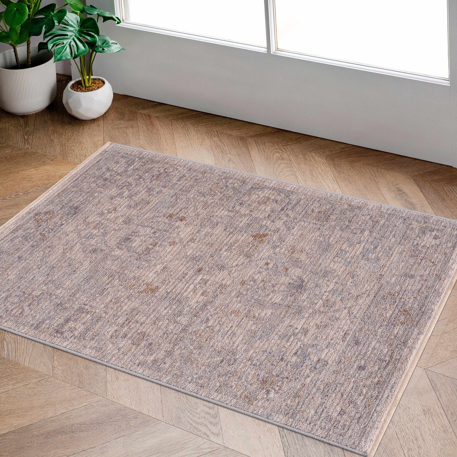 Entryway scene with the Ayarn Thick Luxe Statement Rug in brown, charcoal, and gray on wood floors near a white door and potted plants. Roomscene-Rectangle