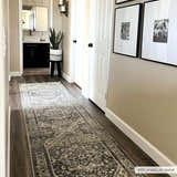Hallway scene with dark wood floors and the gray Ailsa Area Rug runner. Neutral walls, white doors, and framed art create a cozy feel. Roomscene-Runner
