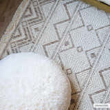 Close-up of the Armen Area Rug, a beige and cream rug with a geometric diamond pattern and fringe detail. Styleshot