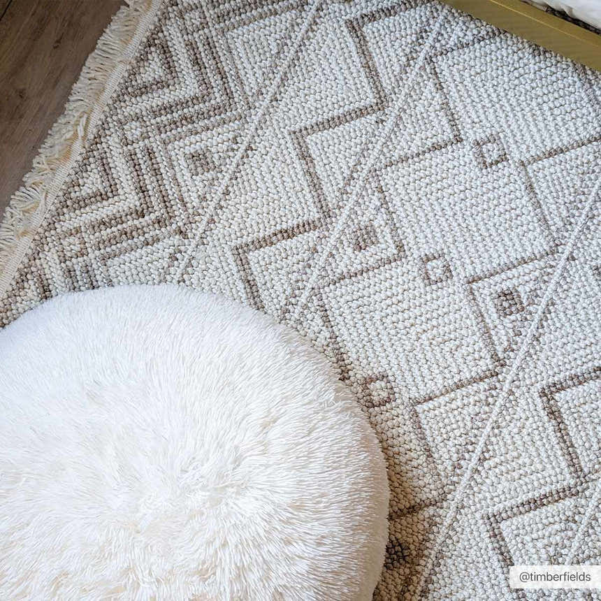 Close-up of the Armen Area Rug, a beige and cream rug with a geometric diamond pattern and fringe detail. Styleshot