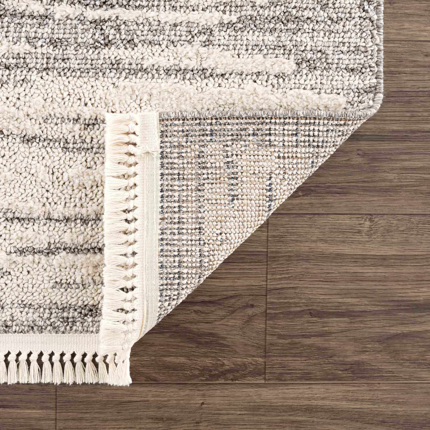 Close up of Lave Bone & Taupe Area Rug showing its bone and taupe striped design, fringe detail, and machine-woven construction. Fold