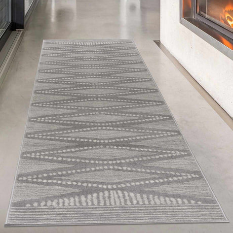 A gray and ivory colored geometric patterned area rug displayed in a modern interior setting with Hardwood flooring.