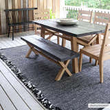 Outdoor dining area with a Boyden Black Area Rug with Tassels, wood table and chairs, and a black bench. Roomscene-Rectangle
