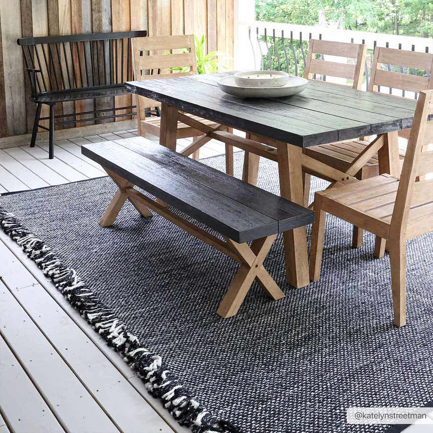 Outdoor dining area with a Boyden Black Area Rug with Tassels, wood table and chairs, and a black bench. Roomscene-Rectangle