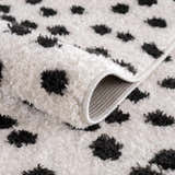 Close-up of the Cansu Black & White Dotted Area Rug showing its shag texture and machine-woven backing. Fold