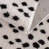 Close-up of the Cansu Black & White Dotted Area Rug, showing its shag texture, black spots, and woven backing. Fold
