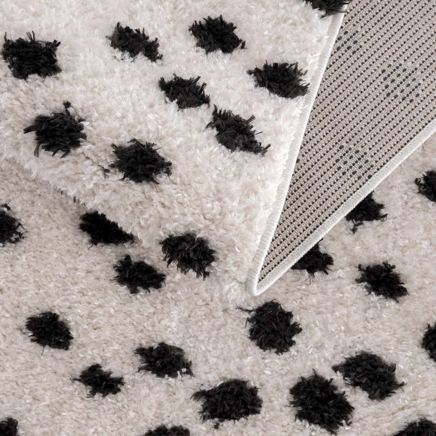 Close-up of the Cansu Black & White Dotted Area Rug, showing its shag texture, black spots, and woven backing. Fold