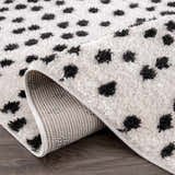 Close up of the Cansu Black & White Dotted Area Rug showing the shag texture and backing. Fold