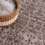 Close-up of the Lugo Luxe Area Rug in light gray with a traditional floral pattern and a basket with a white fluffy blanket. Swatch
