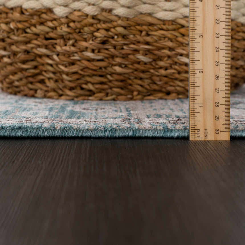 Close-up of Edremit Area Rug edge showing light sage, cream, and brown pattern, plus rug thickness with ruler. Pile