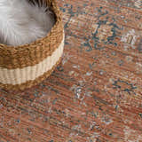 Close-up of the Mele Area Rug. Burnt orange, beige, and blue tones with a traditional pattern. Wicker basket with white fur. Styleshot