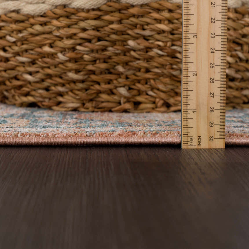 Close-up of the Mele Area Rug showing the pile height with a ruler, next to a woven basket. Colors: bone, burnt orange, and gray. Pile