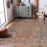 Living room scene with a burnt orange Mele Area Rug, gray dresser, leather pouf, and woven chair. Roomscene-Rectangle