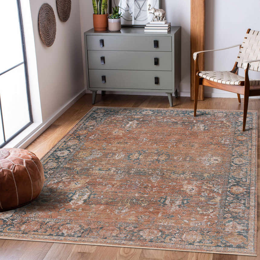 Living room scene with a burnt orange Mele Area Rug, gray dresser, leather pouf, and woven chair. Roomscene-Rectangle