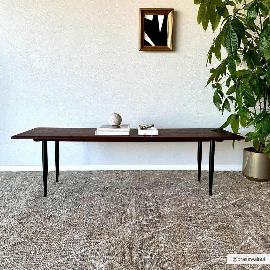 Living room scene with a Carine Jute Area Rug under a dark wood table and potted plant. Neutral tones. Roomscene-Rectangle