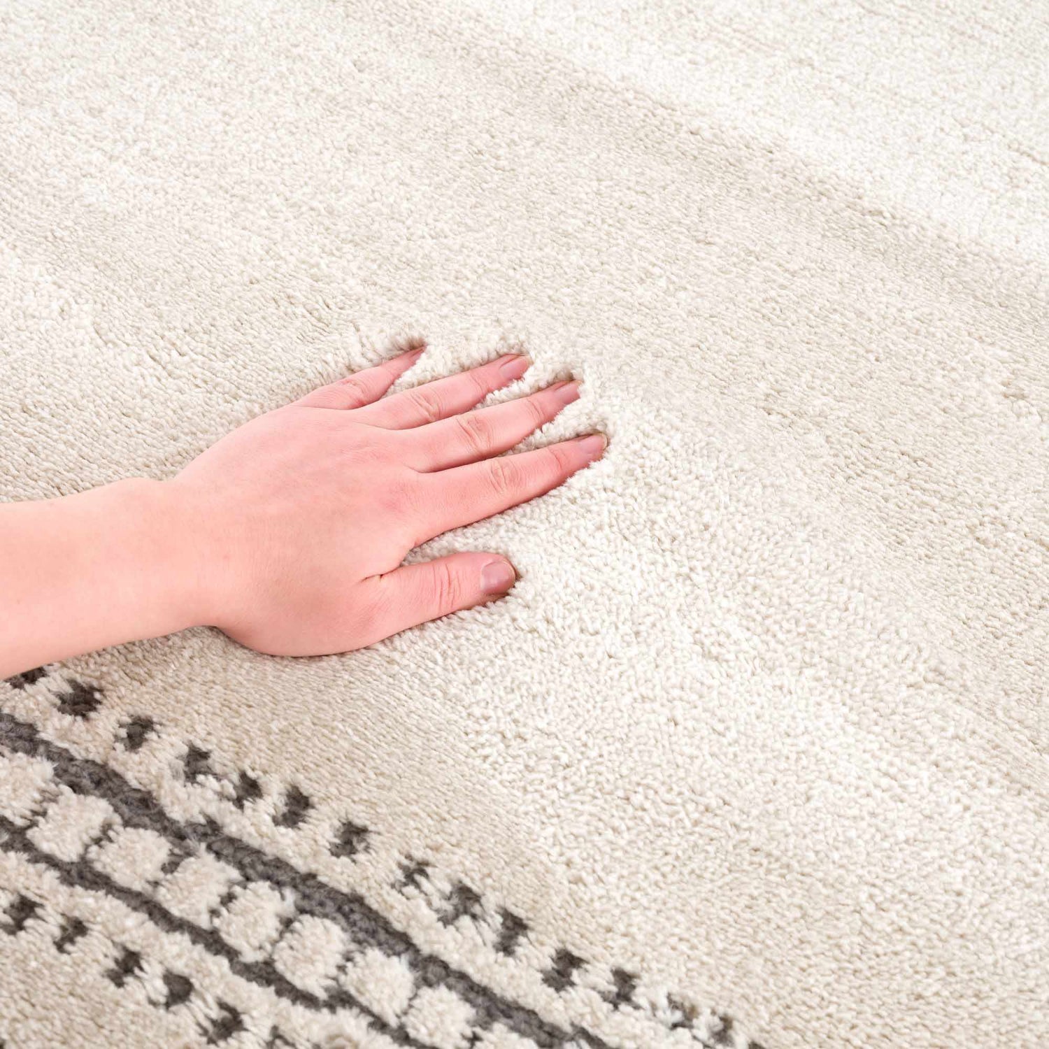 Close-up of the Ryuu Ivory & Gray Area Rug showing its plush texture and geometric gray pattern. Hand pressing into the rug. Texture