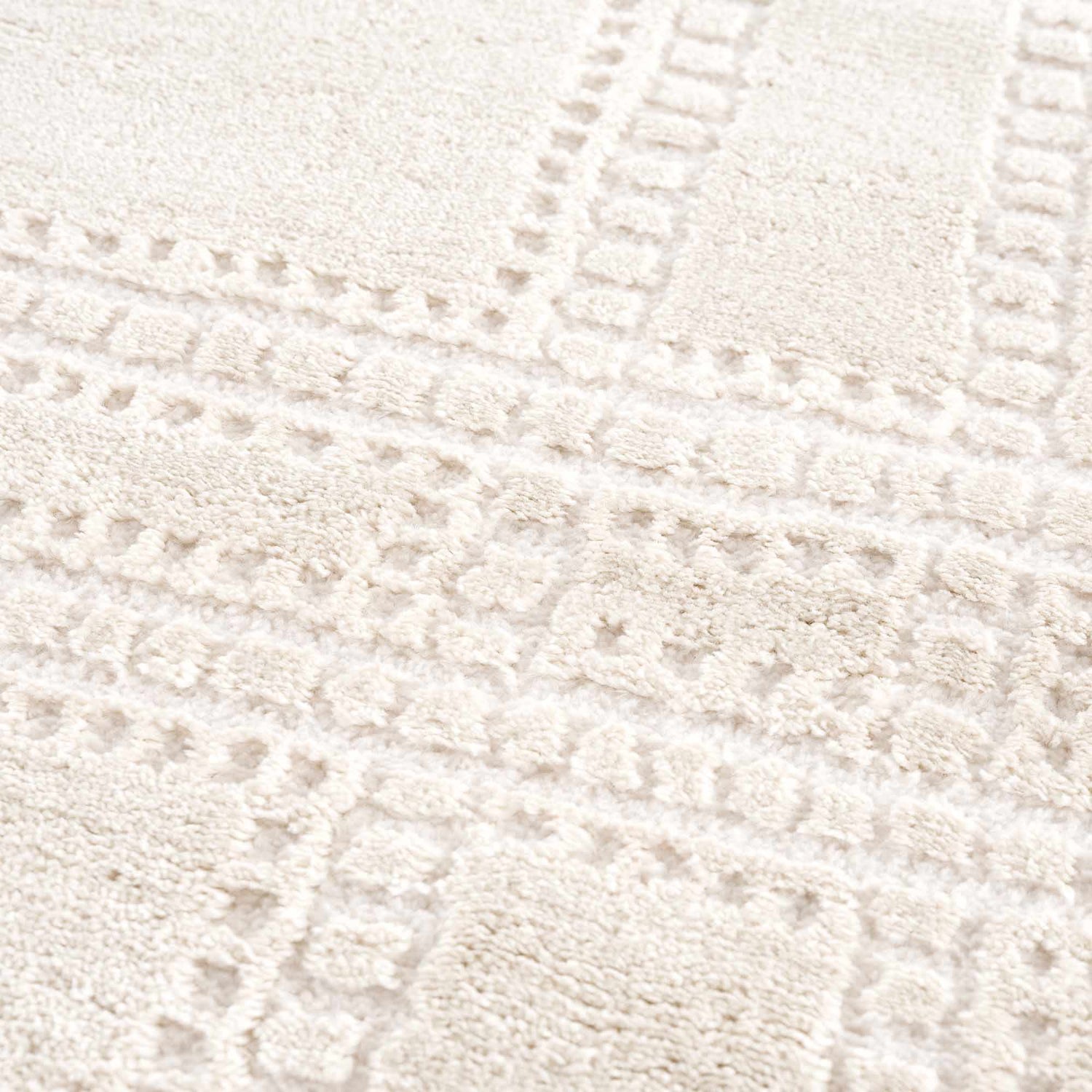 Close-up of the Ryuu Ivory Carved Area Rug showing its plush pile and subtle geometric pattern in cream and beige tones. Texture