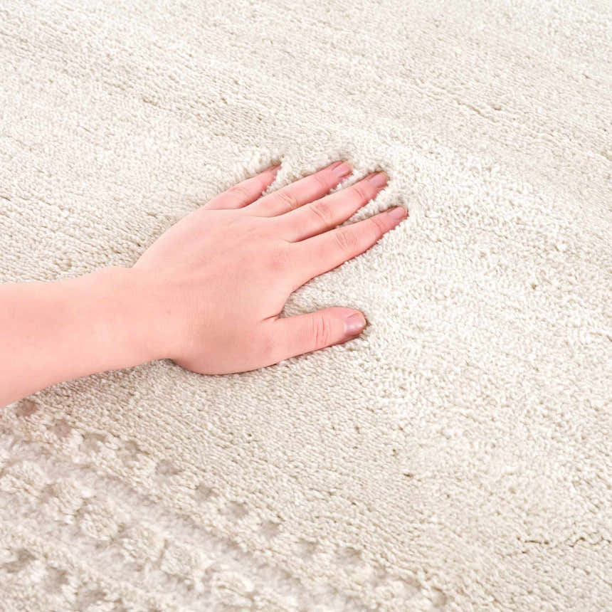 Close-up of the Ryuu Ivory Carved Area Rug showing the soft, plush texture and subtle carved design. Hand touching the rug. Texture