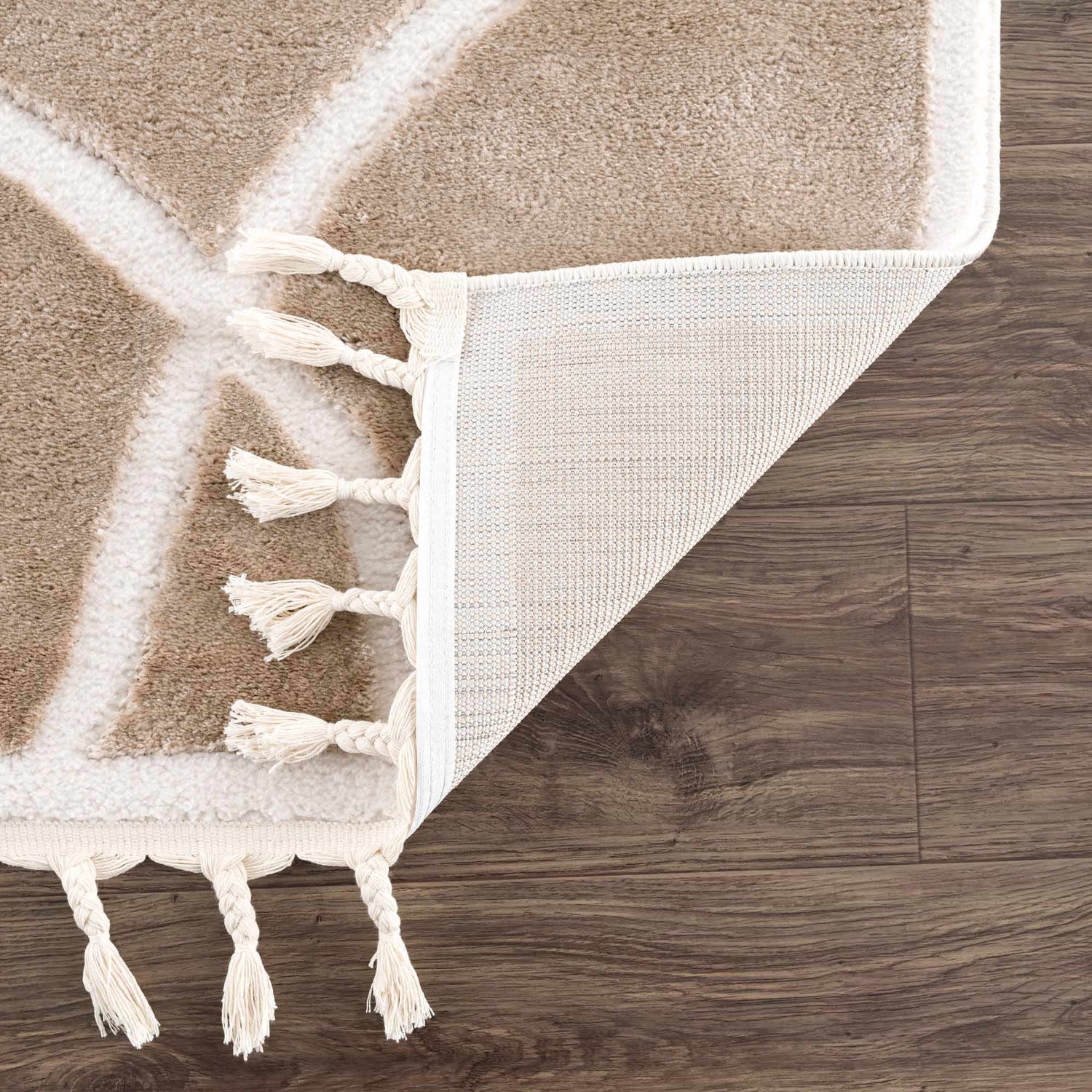 Close-up of the Azana Cream Area Rug showing geometric pattern, tassels, and the rug's backing on dark wood floor. Fold