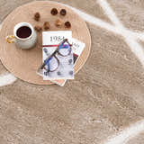 Close-up of the cream Azana Area Rug featuring an abstract geometric design, styled with a book, glasses, and coffee. Styleshot