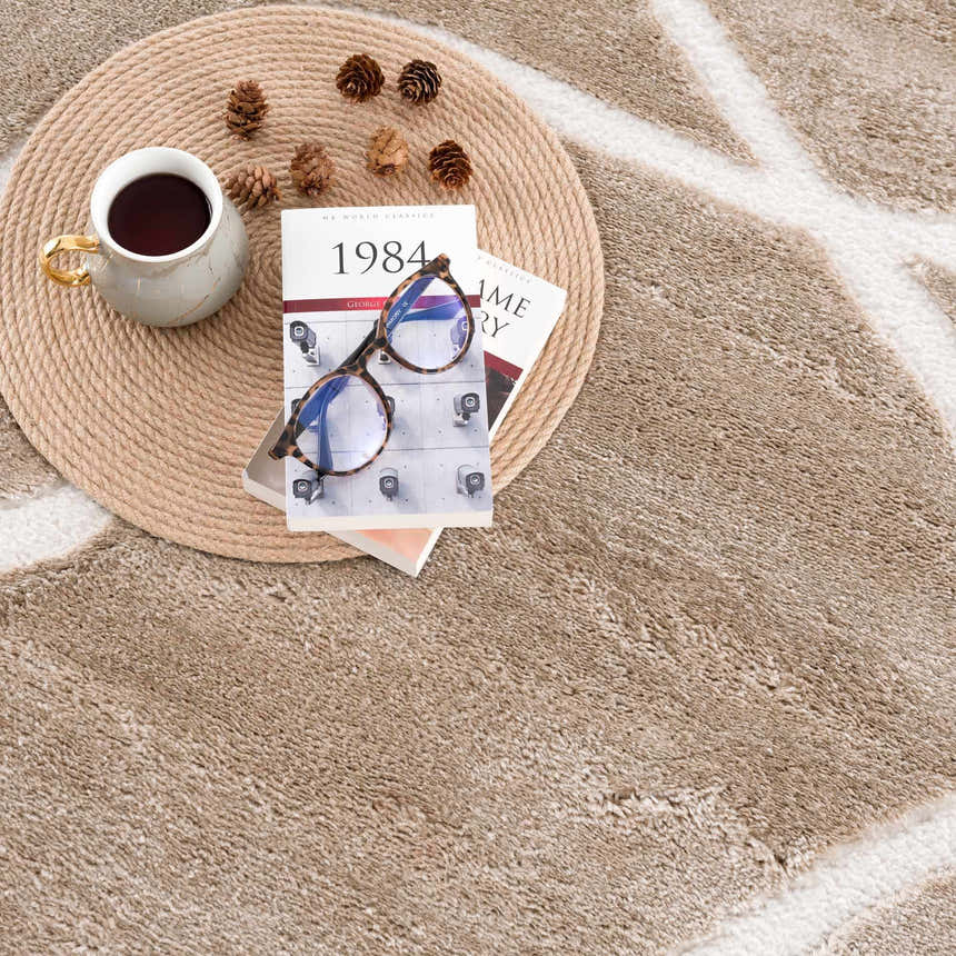 Close-up of the cream Azana Area Rug featuring an abstract geometric design, styled with a book, glasses, and coffee. Styleshot