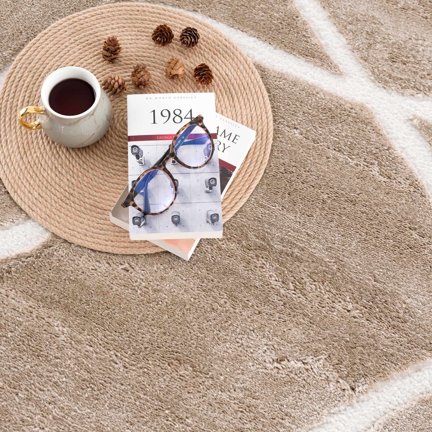 Close-up of the cream Azana Area Rug featuring an abstract geometric design, styled with a book, glasses, and coffee. Styleshot