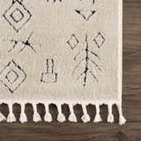Close up of the Thian Tribal Area Rug showing its beige color, black tribal pattern, and knotted fringe. Corner