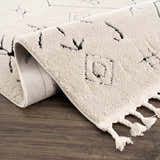 Close-up of the Thian Tribal Area Rug in beige with black geometric designs and braided tassels. Fold