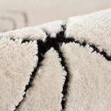 Close-up of the Thian Tribal Area Rug. Beige rug with a thick, plush pile and bold black geometric pattern. Fold