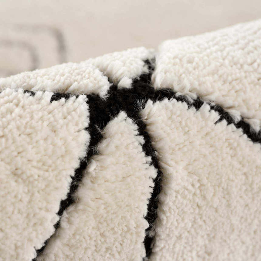 Close-up of the Thian Tribal Area Rug. Beige rug with a thick, plush pile and bold black geometric pattern. Fold