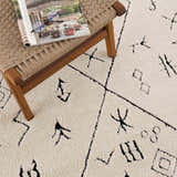 Close-up of the Thian Tribal Area Rug. Beige rug with black Moroccan-inspired geometric patterns and soft, textured pile. Styleshot
