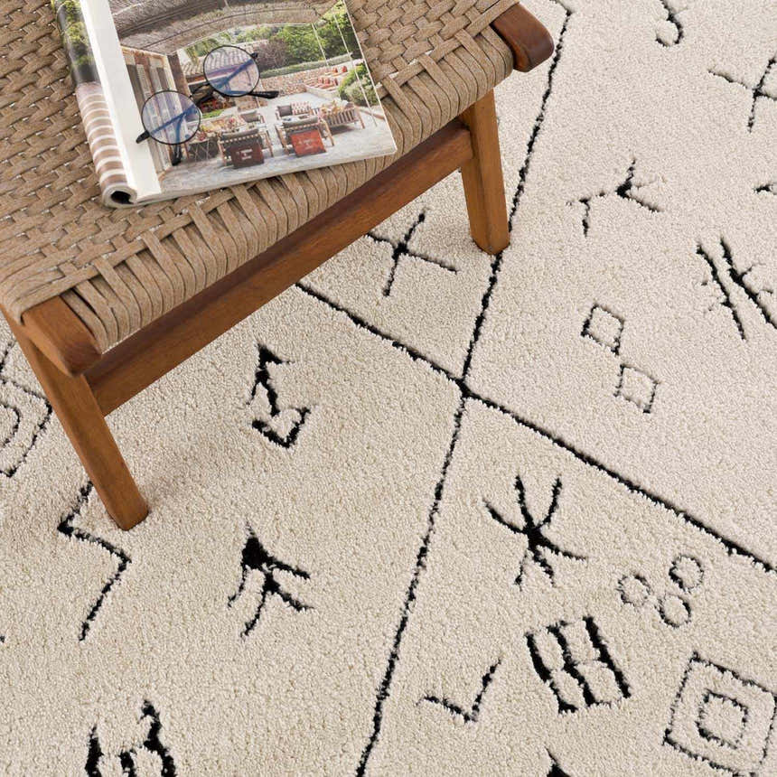 Close-up of the Thian Tribal Area Rug. Beige rug with black Moroccan-inspired geometric patterns and soft, textured pile. Styleshot