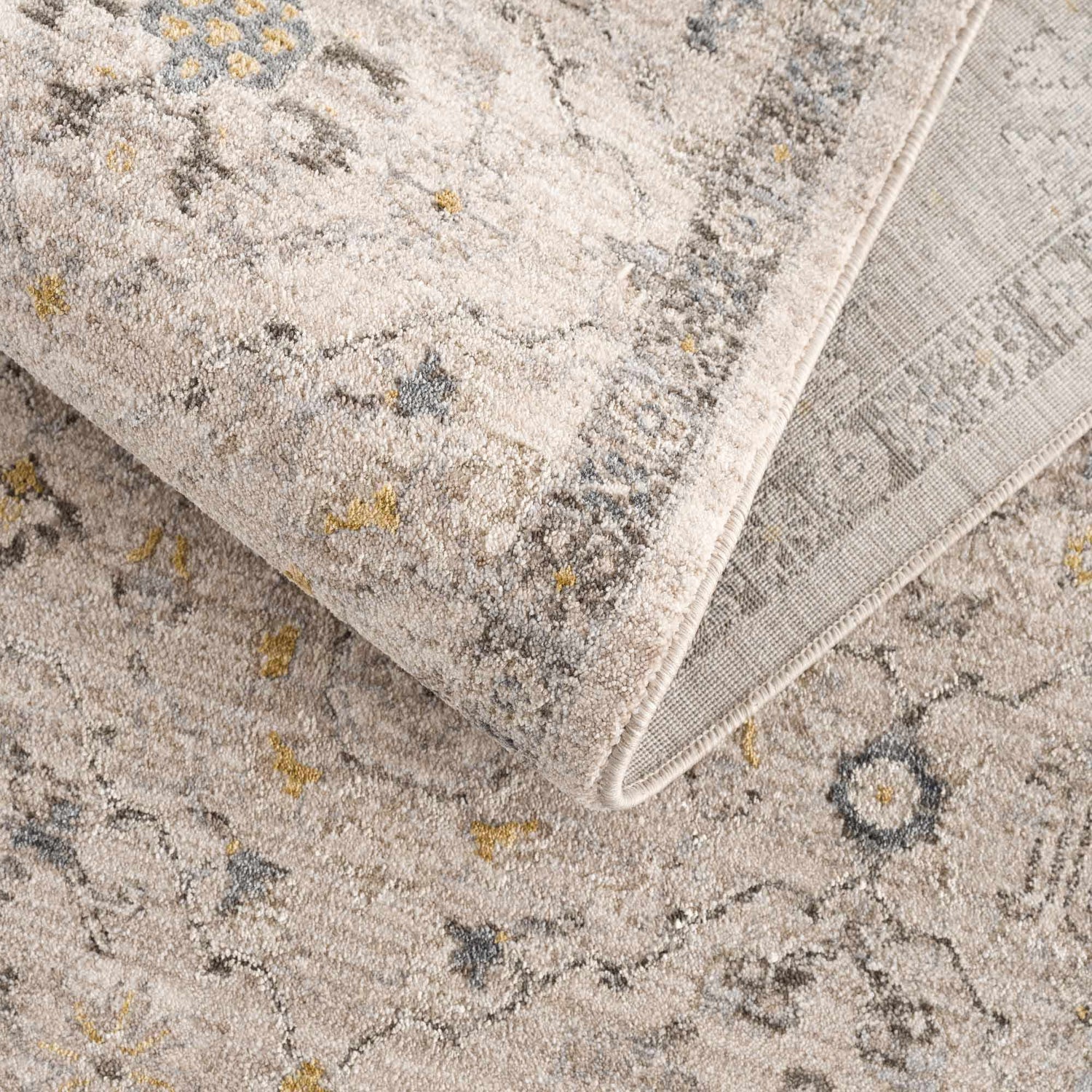Close-up of the Annie Cream Textured Rug. Features a farmhouse style pattern in cream, gray, and gold tones. Fold