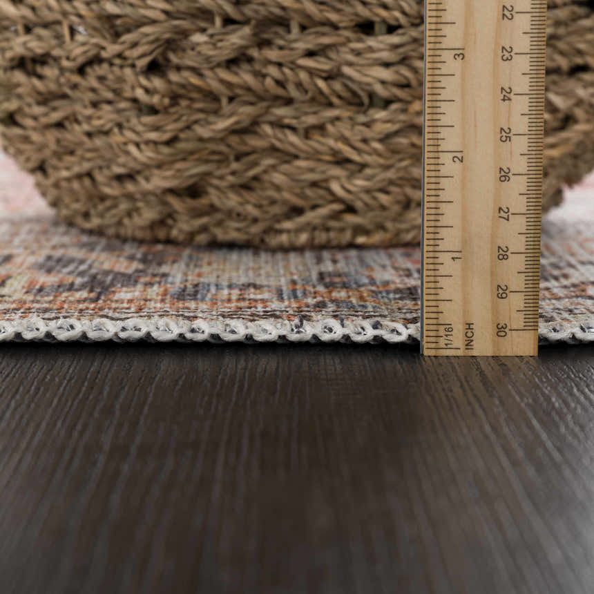 Close-up of Eira Distressed Washable Rug showing texture and pile height with ruler and basket, charcoal, orange, and off-white tones. Pile
