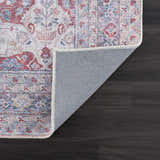 Close-up of the Rust Goma Vintage Area Rug showing blush, red, and blue floral pattern and gray backing on dark wood floor. Fold
