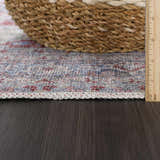 Close-up of Rust Goma Vintage Area Rug showing blush, brick red, and blue pattern with decorative edge on dark wood floor. Pile