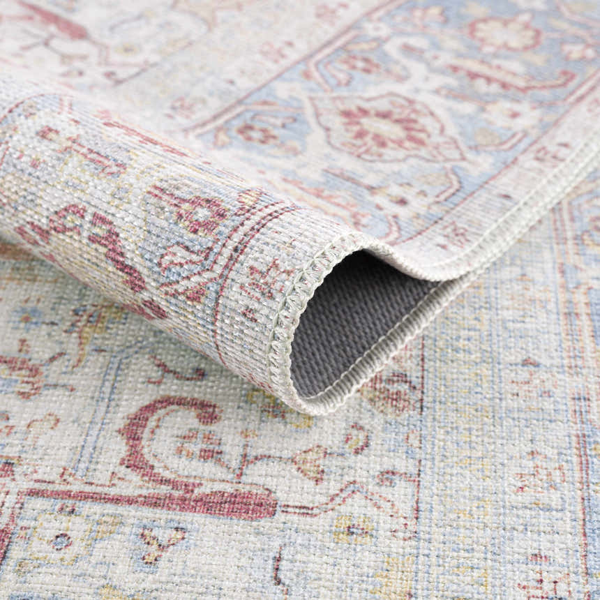 Close-up of the Cream Rust Leeston Washable Rug showing its traditional, vintage pattern and brick red, cream, and light blue colors. Fold