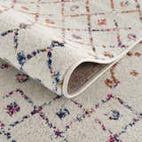 Close-up of the Marash KMRSH-4600 area rug. Off-white rug with blue, red, and orange geometric pattern and rolled edge. Fold