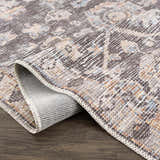 Close-up of the Okoth Area Rug showing its traditional pattern, brown, tan, and blue colors, and machine-woven texture. Fold