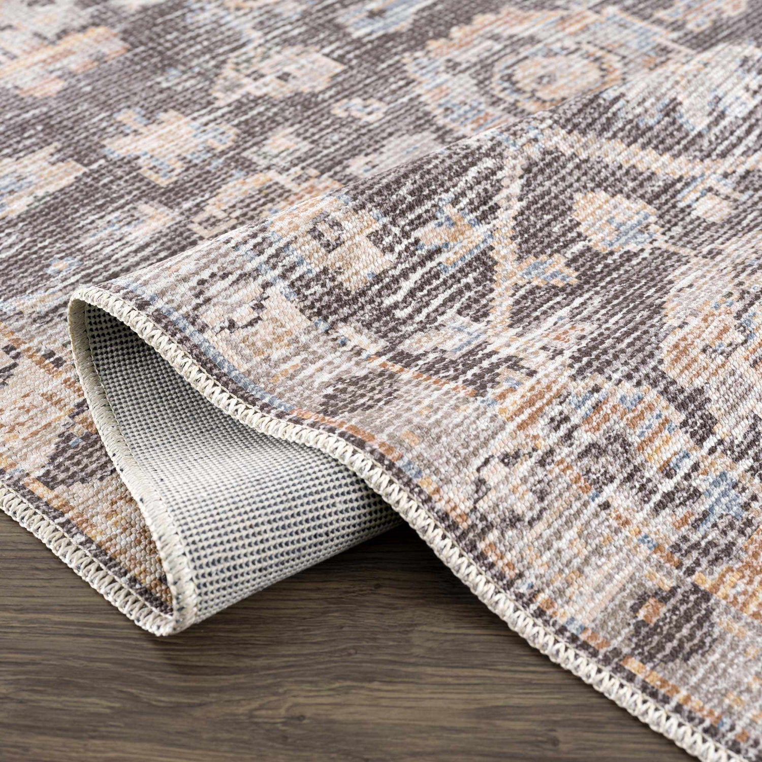 Close-up of the Okoth Area Rug showing its traditional pattern, brown, tan, and blue colors, and machine-woven texture. Fold