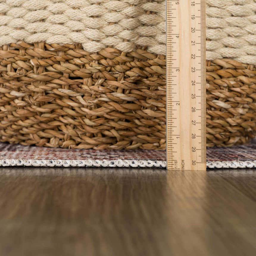 Close-up of the Okoth Area Rug showing the rug's edge, pile height, and woven texture next to a ruler and a wicker basket. Pile