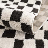 Close-up of the plush Lajos Black & White Checkered Rug, showing the texture and geometric pattern. Fold