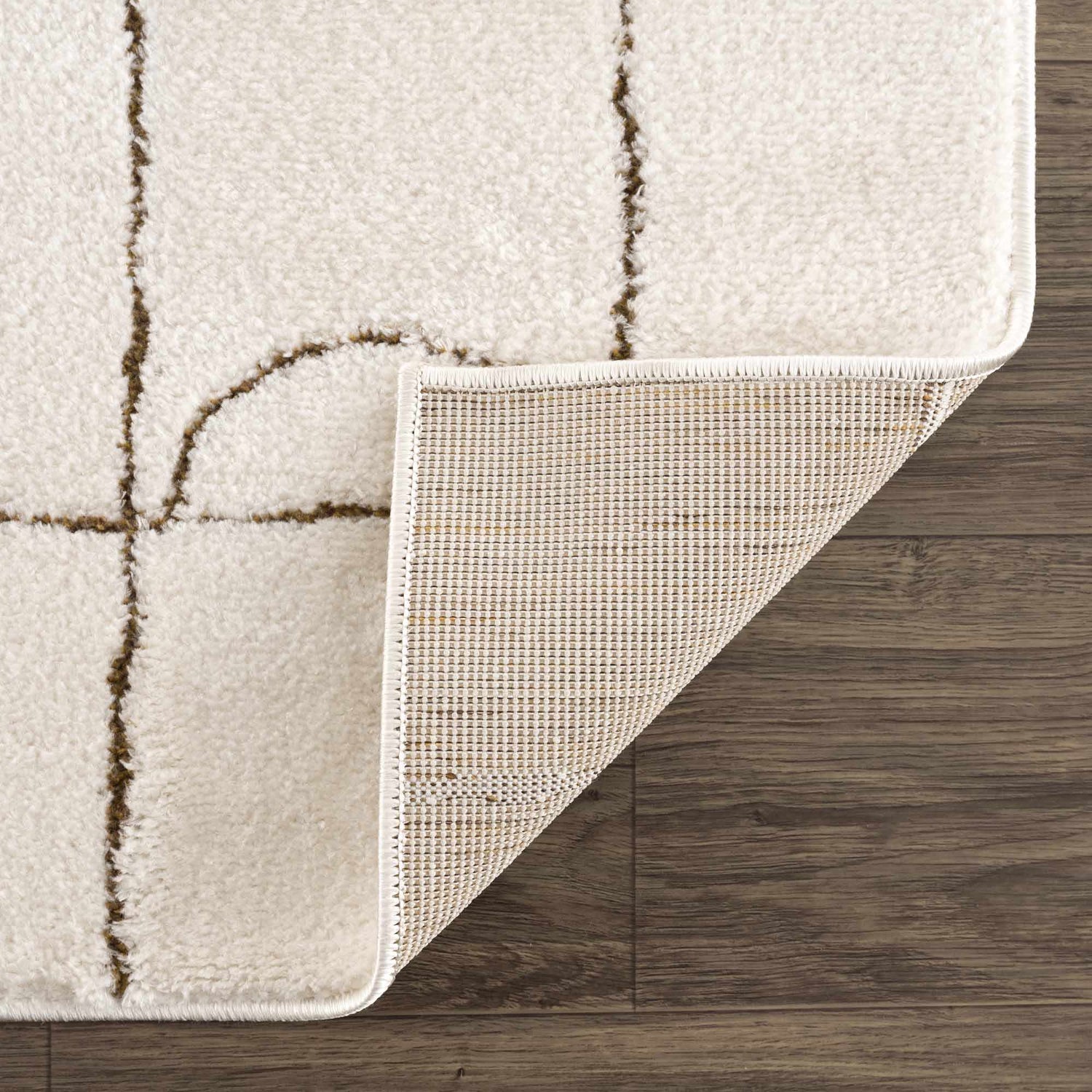 Close-up of the Keanu Area Rug showing its off-white plush texture, brown geometric pattern, and the rug's backing. Fold