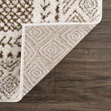 Close-up of the Julio Scandi Boho Area Rug in brown, beige, and ivory on a dark wood floor, showing the rug's backing. Fold