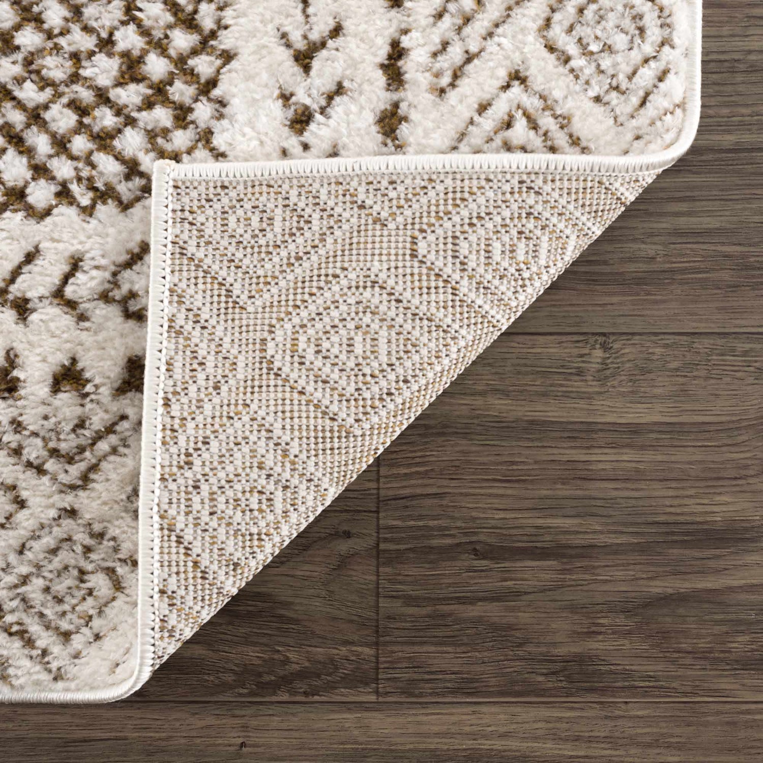 Close-up of the Julio Scandi Boho Area Rug in brown, beige, and ivory on a dark wood floor, showing the rug's backing. Fold