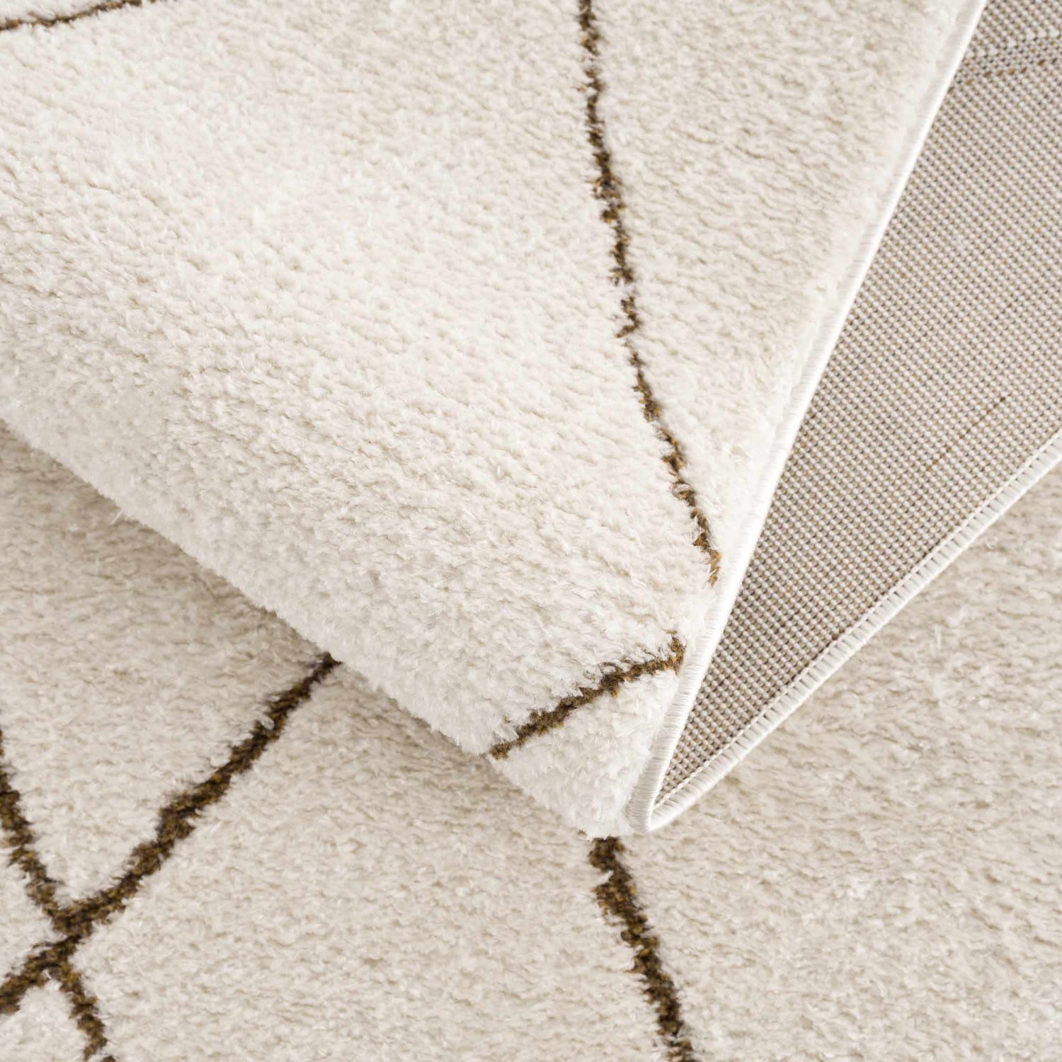 Close-up of the Keone Area Rug showing its soft, beige pile, brown geometric pattern, and durable backing. Fold