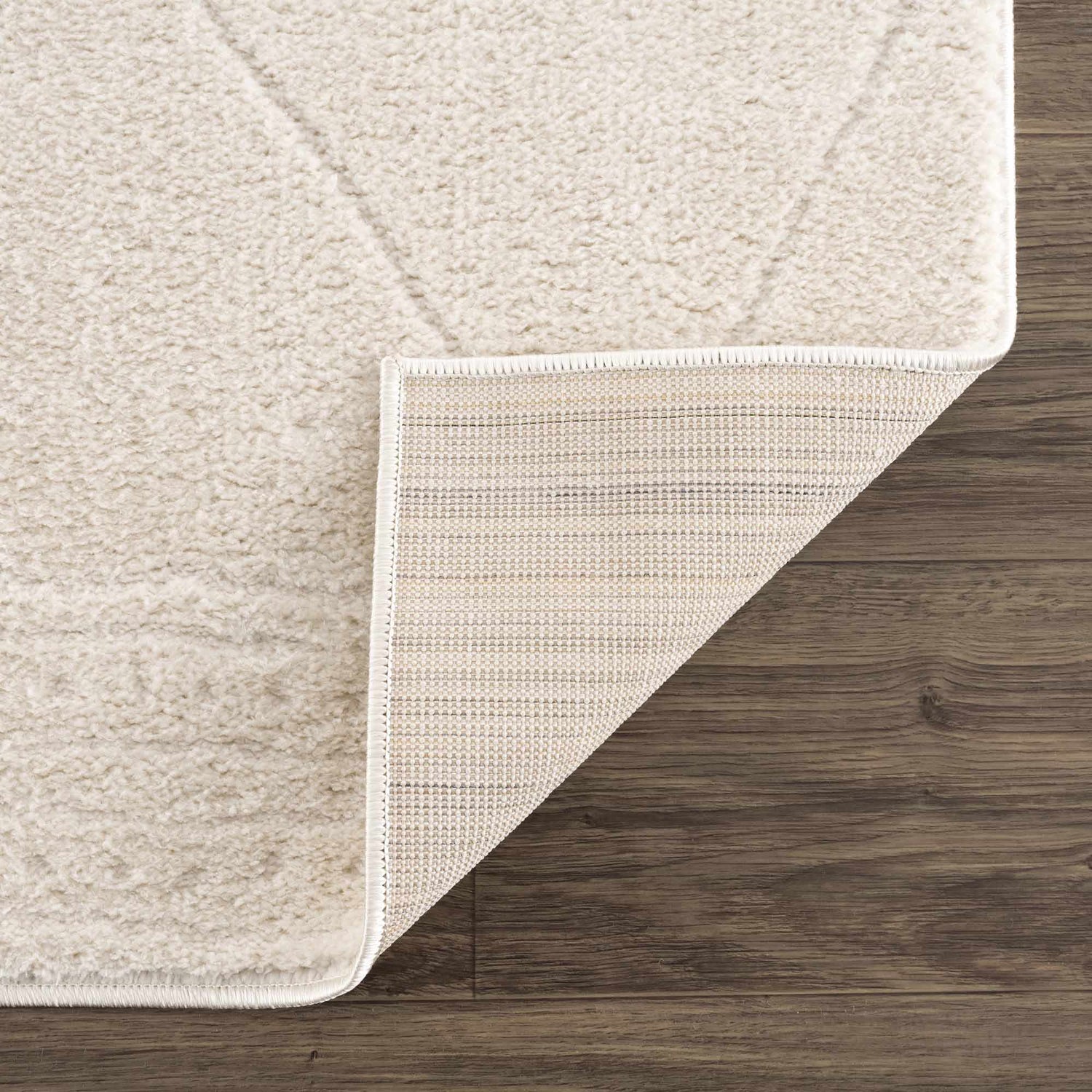 Close up of Keone Ivory Area Rug showing the plush pile, geometric pattern, and backing on dark wood floors. Fold