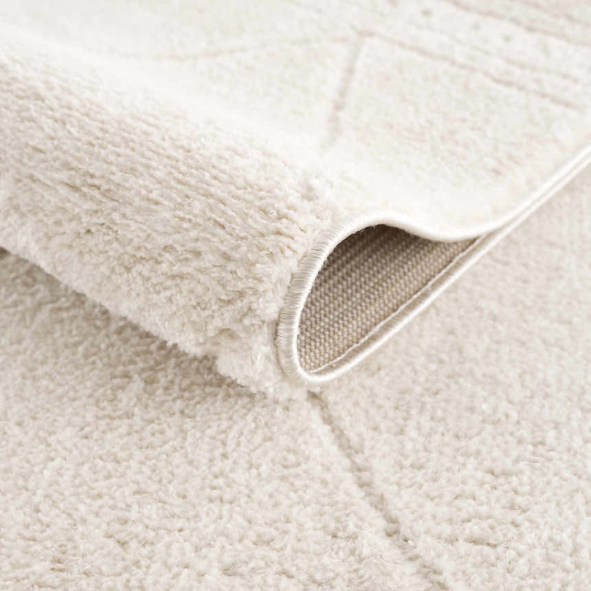 Close-up of the Keone Ivory Area Rug showing its plush texture, cream color, and machine-woven construction. Fold